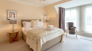 A bedroom with a large bed, two bedside tables, a chandelier, and a window with curtains. - JOIVY Inviting Apartment near Leith Walk (Edinburgh)