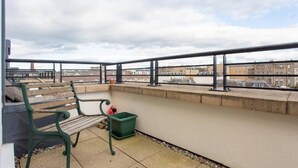 A balcony with a bench, a green trash bin, and a view of buildings. - JOIVY Inviting Apartment near Leith Walk (Edinburgh)