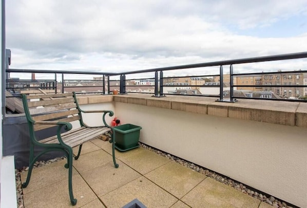 A balcony with a bench, a green trash bin, and a view of buildings. - JOIVY Inviting Apartment near Leith Walk (Edinburgh)