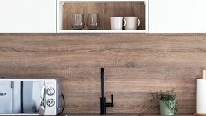 A kitchen with a built-in microwave, a sink, and a wooden cabinet above it containing plates, glasses, and cups. - Horizon: A Modern Luxury Studio (London)