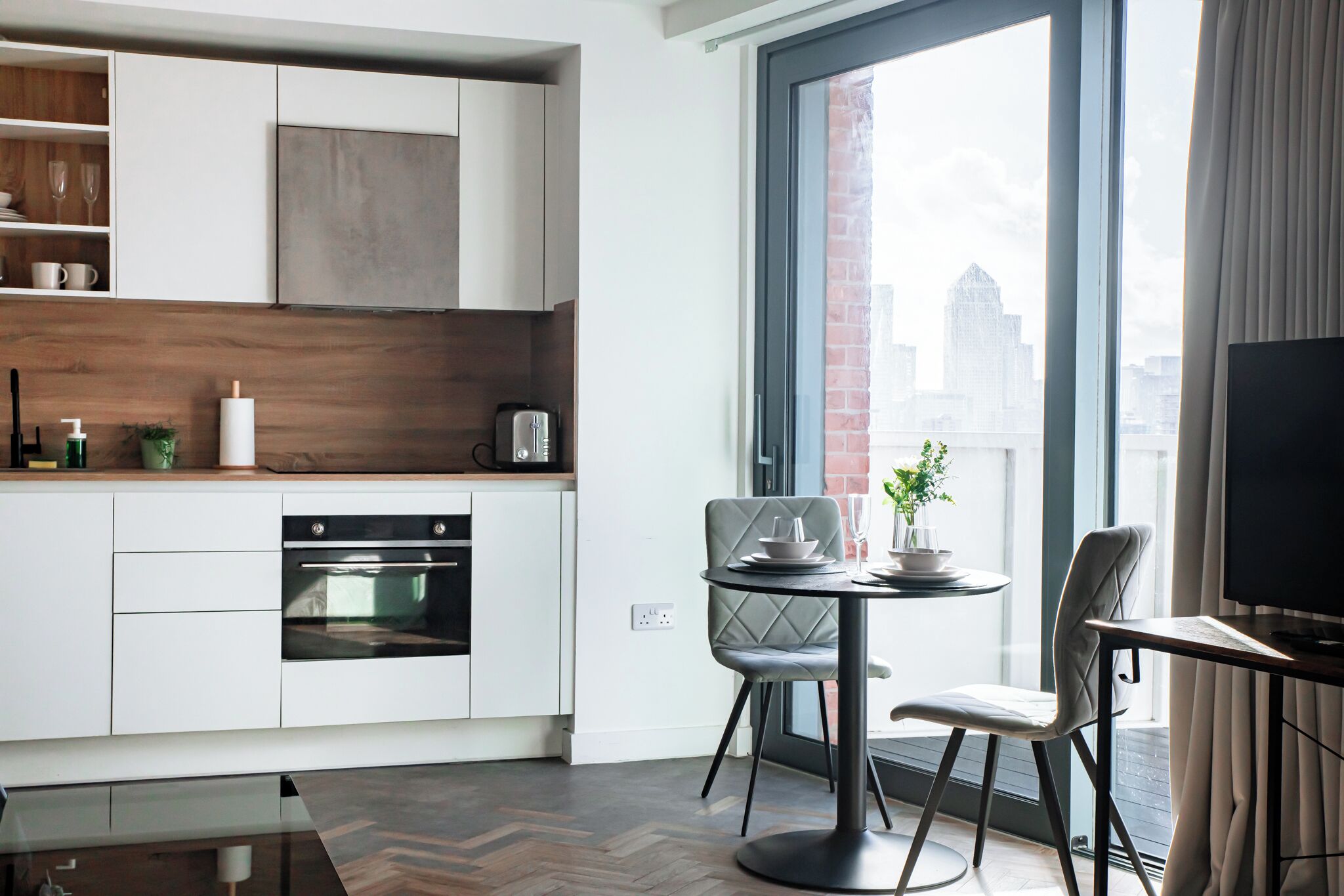 Eine moderne Küche mit weißen Schränken, einem eingebauten Backofen und einem Essbereich mit rundem Tisch und zwei Stühlen.