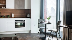 A modern kitchen with white cabinets, a built-in oven, and a dining area with a round table and two chairs. - Horizon: A Modern Luxury Studio (London)