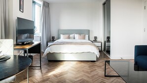 A modern hotel room with a large bed, a desk with a flat-screen TV, a glass coffee table, and a blue armchair. - Horizon: A Modern Luxury Studio (London)