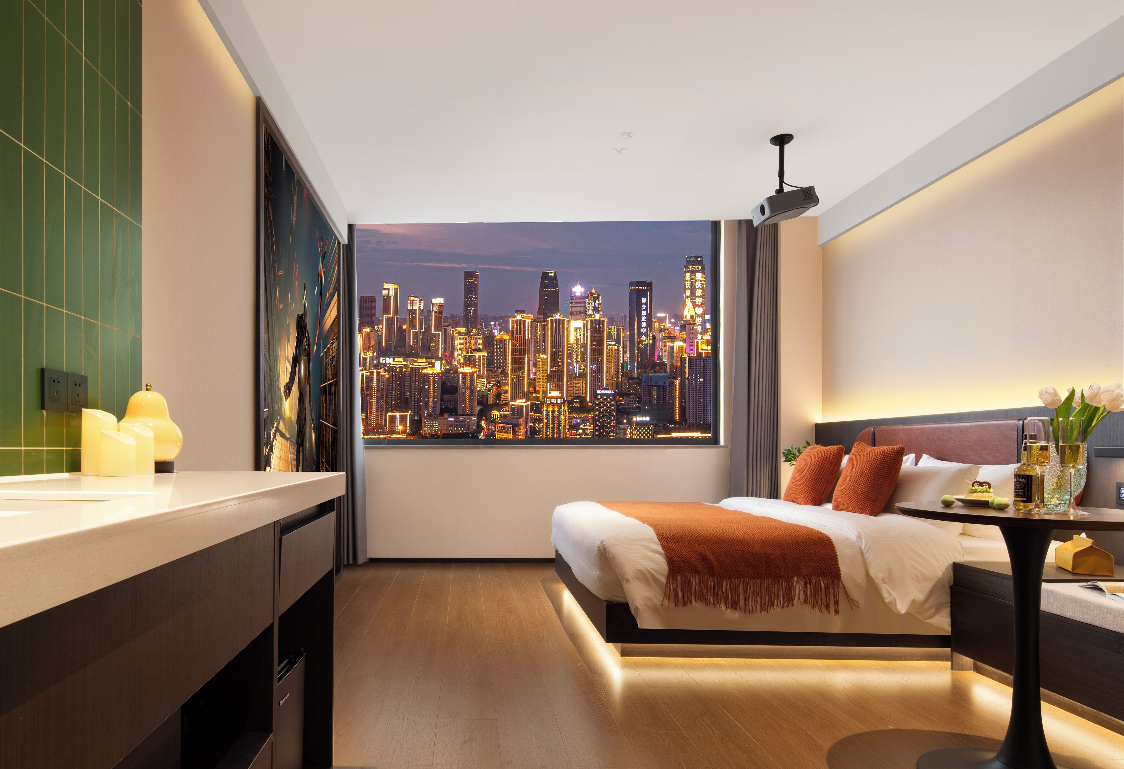 A modern hotel room with a city skyline view, a bed with white bedding and orange pillows, a small table with a vase of flowers, and a nightstand with a lamp.