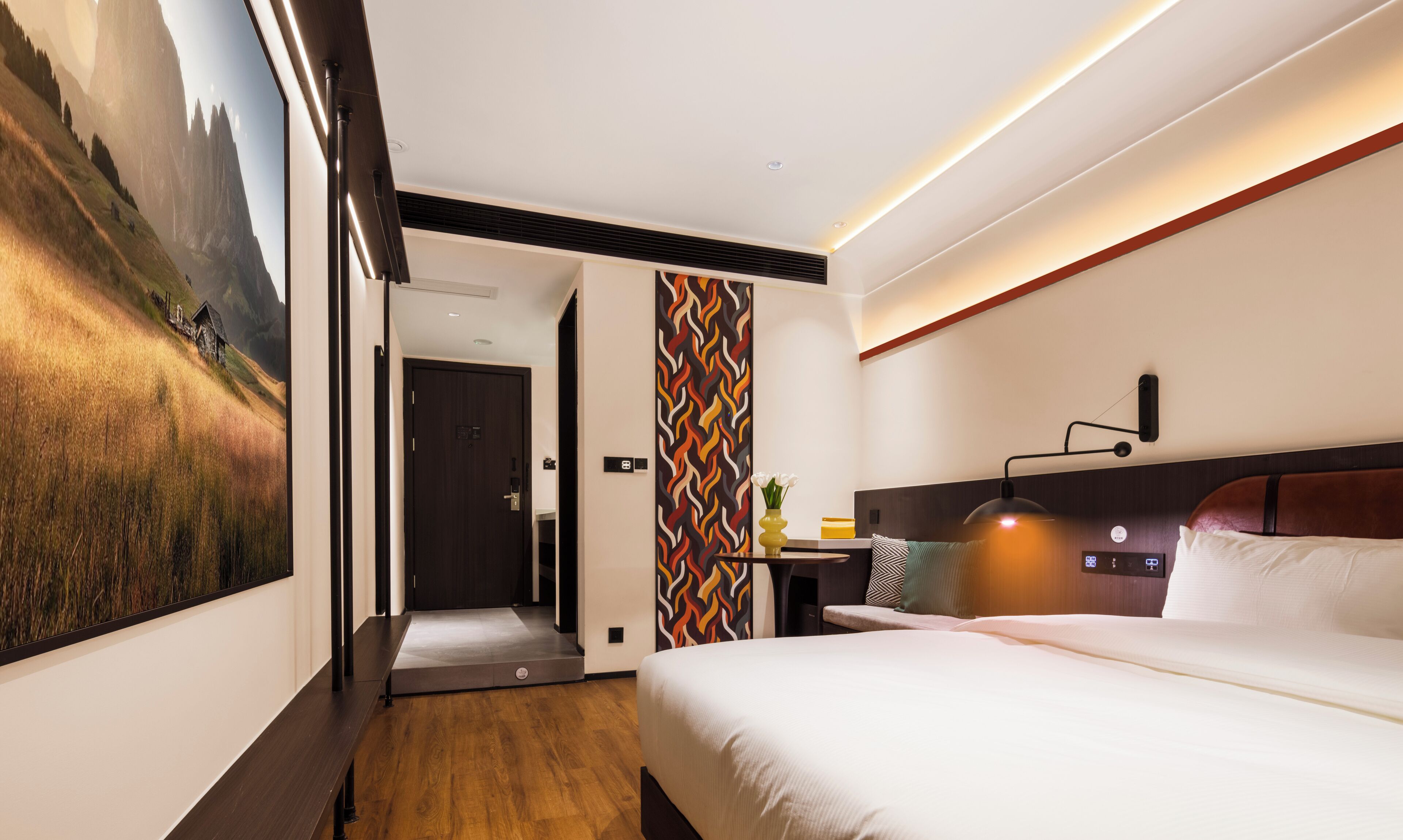 Une chambre d’hôtel moderne, équipée d’un lit, d’une table de chevet, d’une lampe et offrant une vue sur un paysage montagneux grâce à une grande fenêtre.