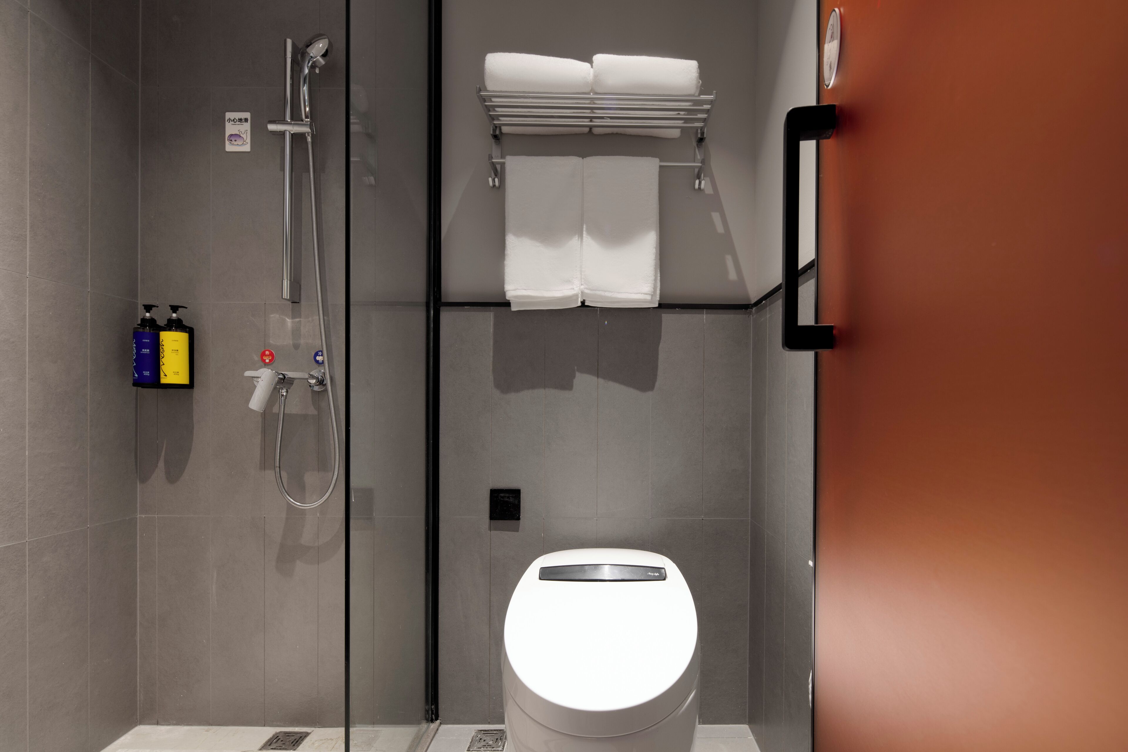 A modern bathroom with a glass-enclosed shower, a toilet, and a towel rack with folded towels.