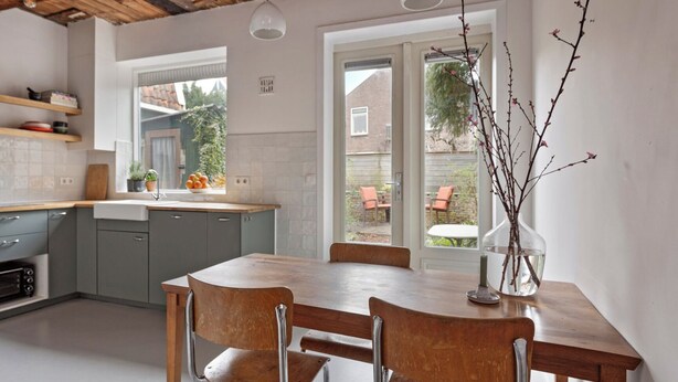 Una cucina con un tavolo e sedie in legno, un lavello e una finestra vista giardino.