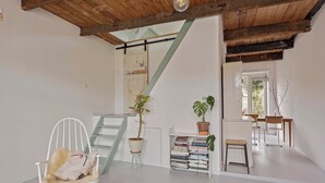 Un'ampia stanza con soffitto in legno, una sedia bianca con cuscino soffice, una scala e una libreria piena di libri.