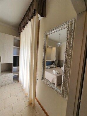 Une chambre d’hôtel avec un grand miroir, un lit doté d’une tête de lit bleue, une table de chevet avec une lampe et une armoire.