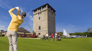 Um campo de golfe com um edifício semelhante a uma torre ao fundo.