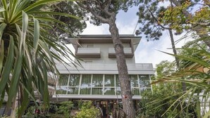 Um edifício moderno com uma escadaria central, rodeado por vegetação exuberante e uma grande árvore.