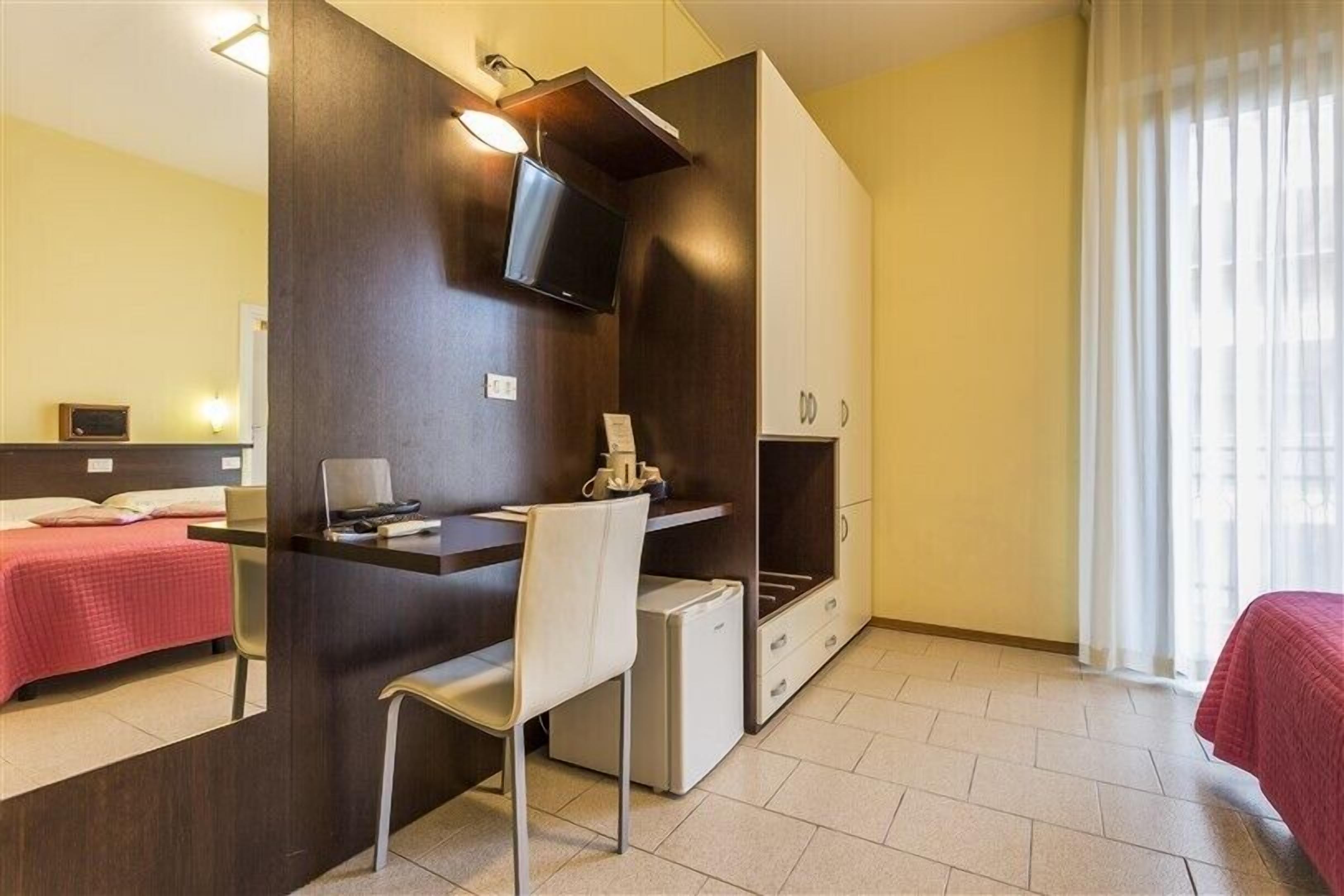 Habitación de hotel compacta con cama, escritorio con silla, televisor y armario.