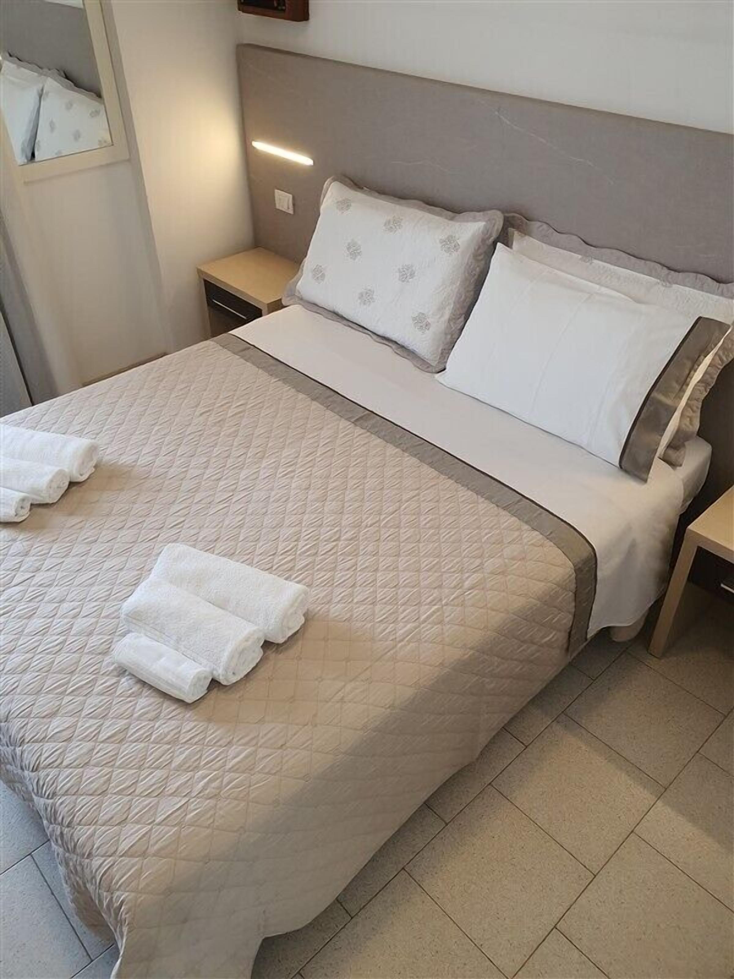 A neatly made bed with a quilted bedspread, two pillows, and two rolled towels on the bed.