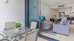 A modern living space with a glass partition separating a dining area with a table and chairs, a grey sofa, and a kitchen area with a television and refrigerator. - Panorama river view with Free Parking (South Brisbane)