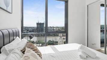A modern bedroom with a large window, a bed with white linens, and a view of a cityscape.