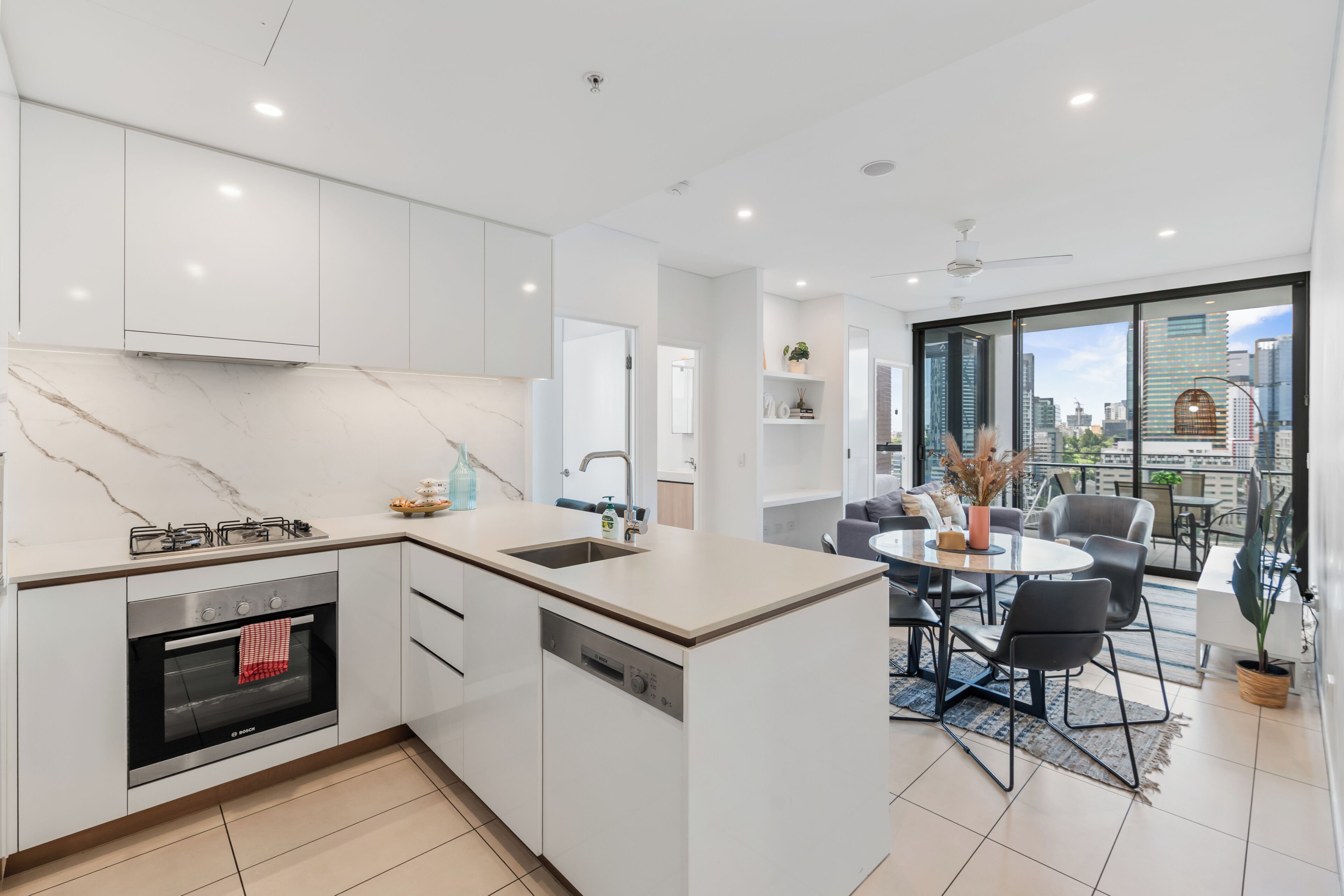 A modern kitchen with a built-in oven, a sink, and a dining area with a round table and chairs.