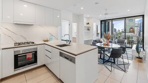 A modern kitchen with a built-in oven, a sink, and a dining area with a round table and chairs. - Panorama river view with Free Parking (South Brisbane)