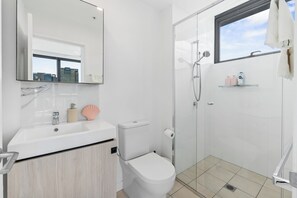 Ein modernes Badezimmer mit Waschbecken, Toilette und Dusche – alles in Weiß.