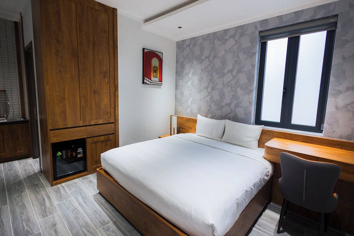 Una habitación de hotel moderna con una cama grande, un escritorio y vistas de la ciudad a través de una ventana.
