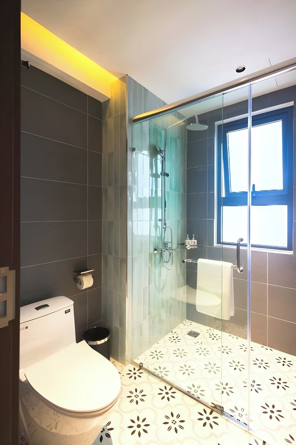 A modern bathroom with a glass-enclosed shower, a toilet, and a patterned floor.