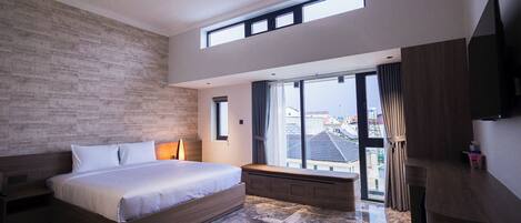 A modern bedroom with a large bed, a bench, a TV, and a view of the city through large windows.