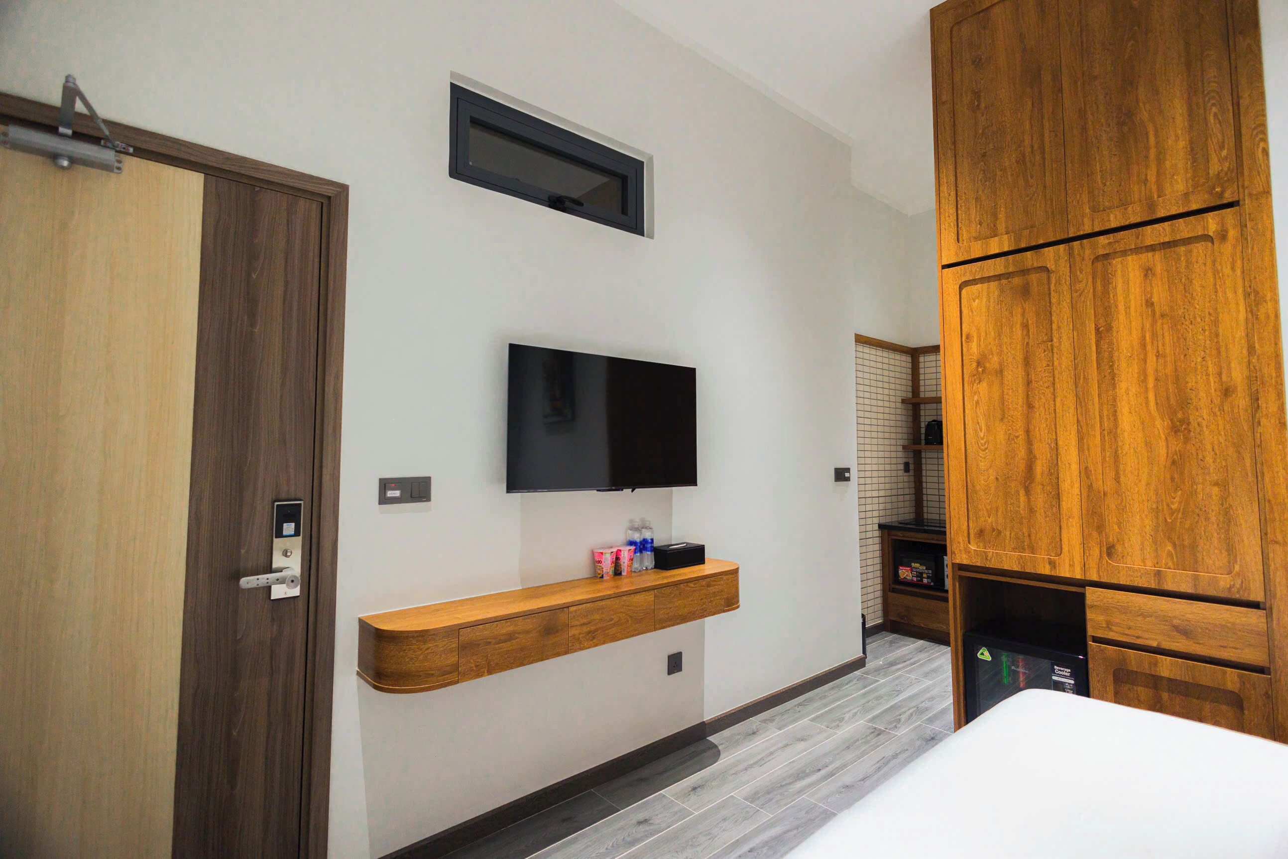 A modern hotel room with a wooden wardrobe, a mounted TV, and a built-in shelf with toiletries.