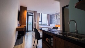 Ett modernt hotellrum med ett litet kök, en matplats och ett stort fönster med gardiner.