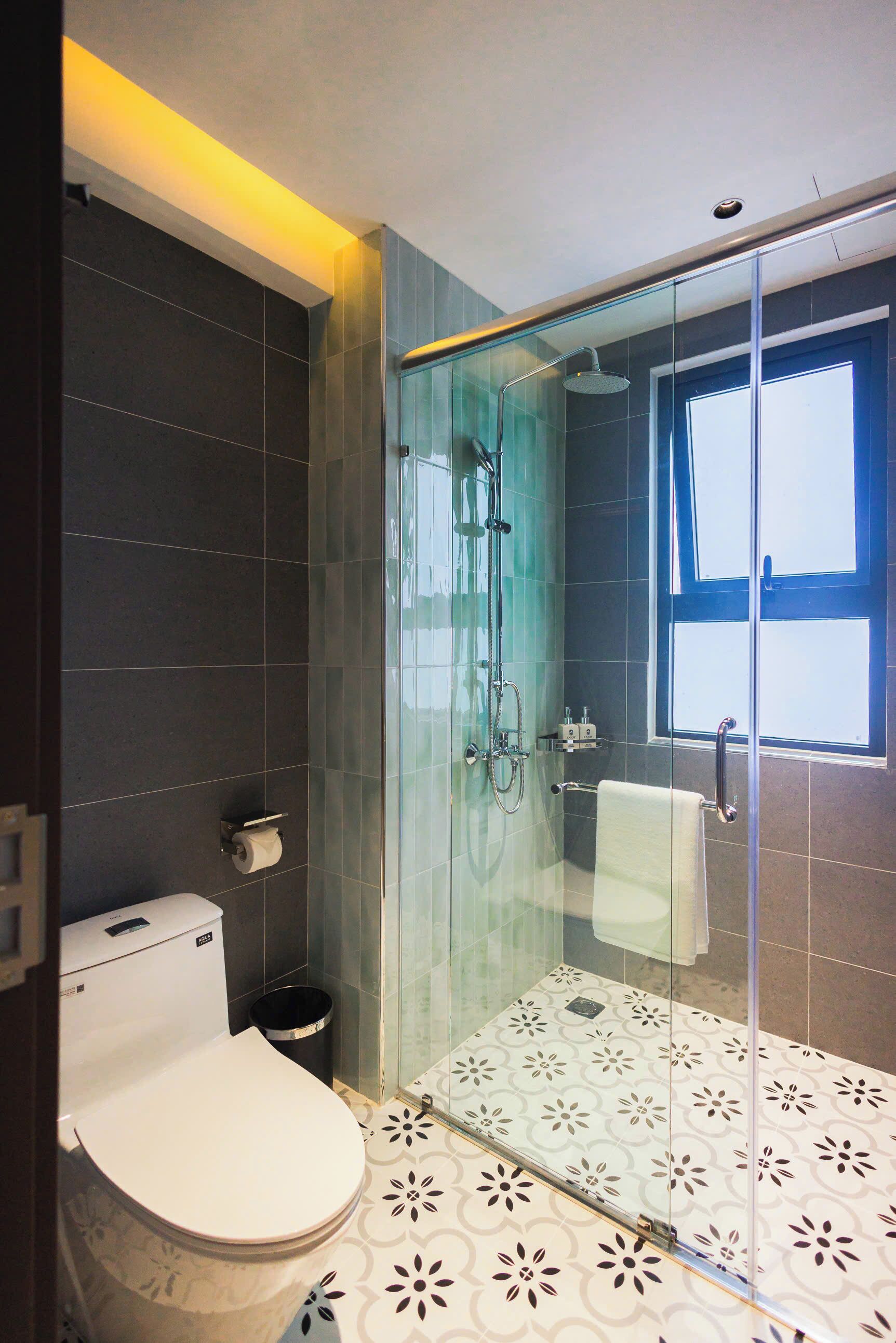 A modern bathroom with a glass-enclosed shower, a toilet, and a patterned floor.