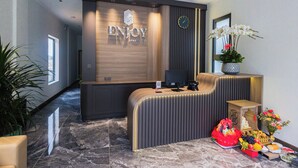 En receptionsdisk med träpanel och en klocka ovanför. Till höger står en krukväxt med vita blommor.