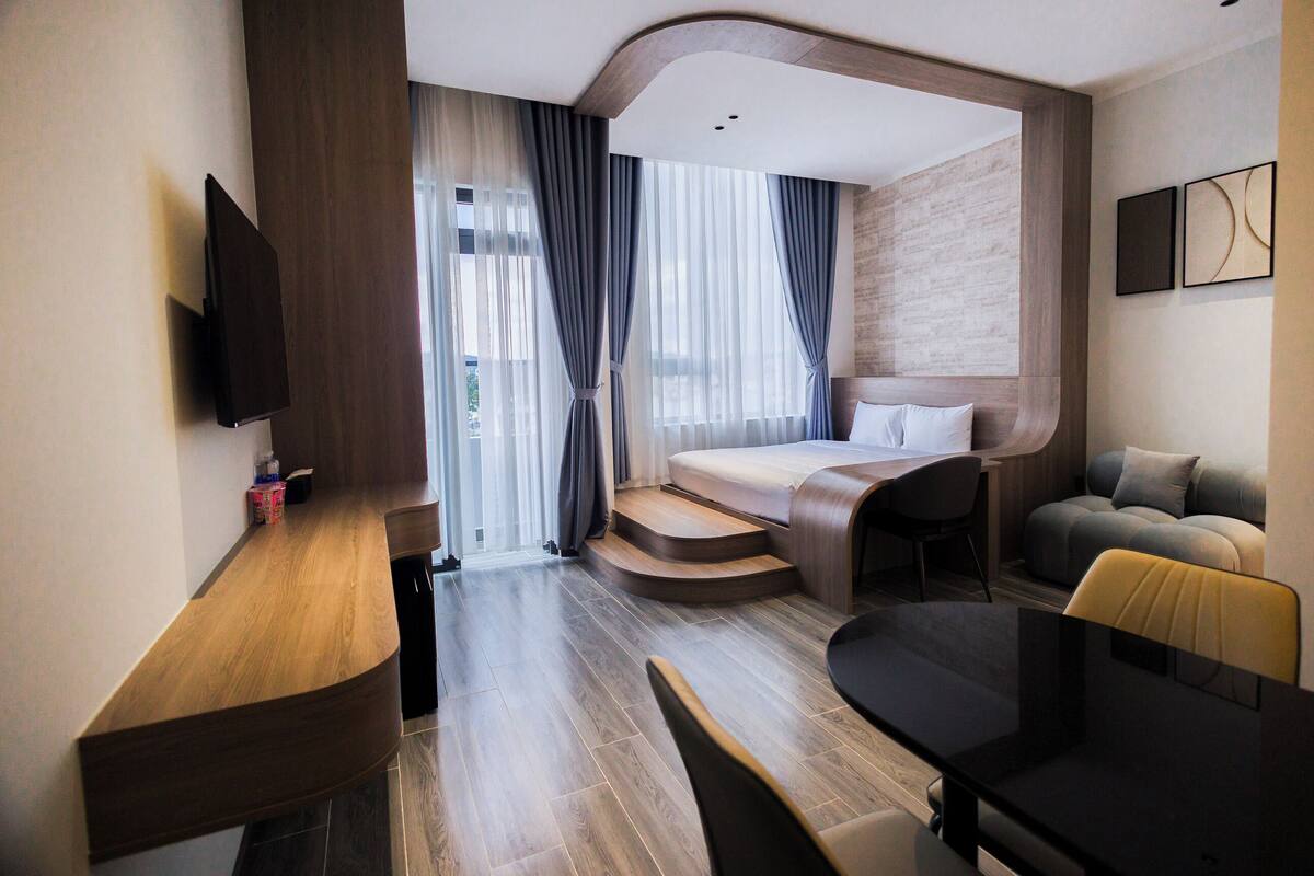 Una habitación de hotel moderna con un escritorio de madera, un televisor de pantalla plana, un sofá, una cama y una escalera que lleva a un balcón al aire libre.