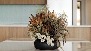 Una cocina moderna con encimera de mármol, un florero negro con flores secas e iluminación colgante.