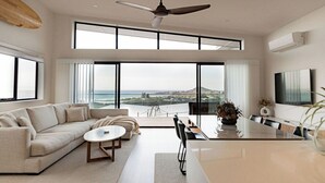 Una sala de estar moderna con un ventanal que ofrece una vista panorámica, un ventilador de techo y un comedor con mesa y sillas.
