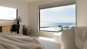 Un dormitorio con un ventanal que ofrece vistas al océano. Hay una cama, un escritorio y una silla.
