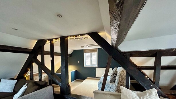 Een gezellig slaapkamer op zolder met zichtbare houten balken, een bed met witte lakens en een blauwe accentmuur.