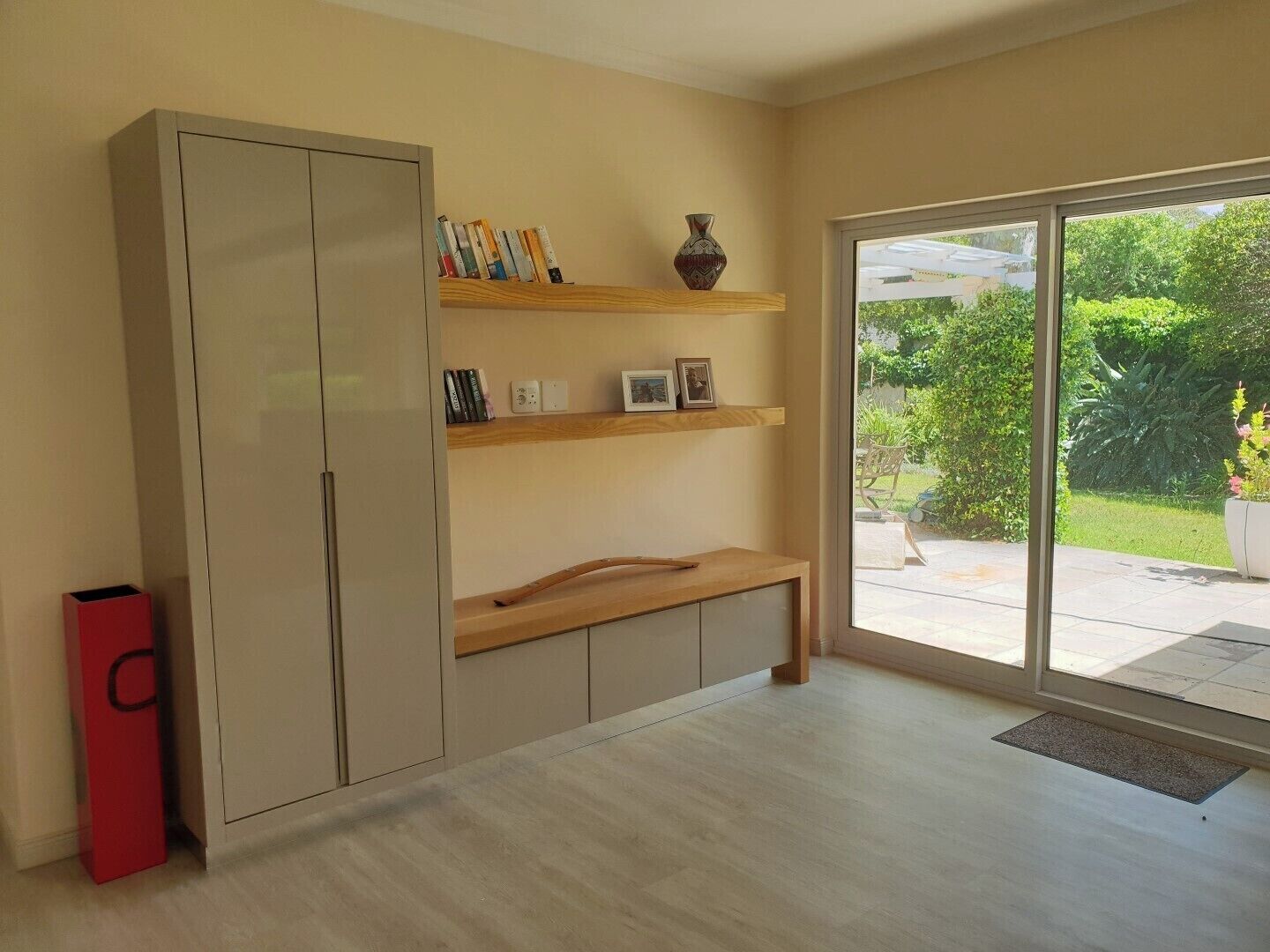 A room with a large wardrobe, a wooden bench, and shelves with books and decorative items.