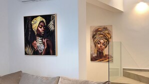 A modern living room with a grey sofa, a staircase, and two framed artworks on the wall.