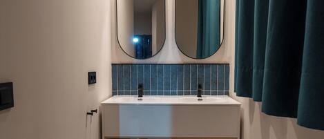 Un baño moderno con un lavamanos blanco, dos espejos y cortinas color turquesa.