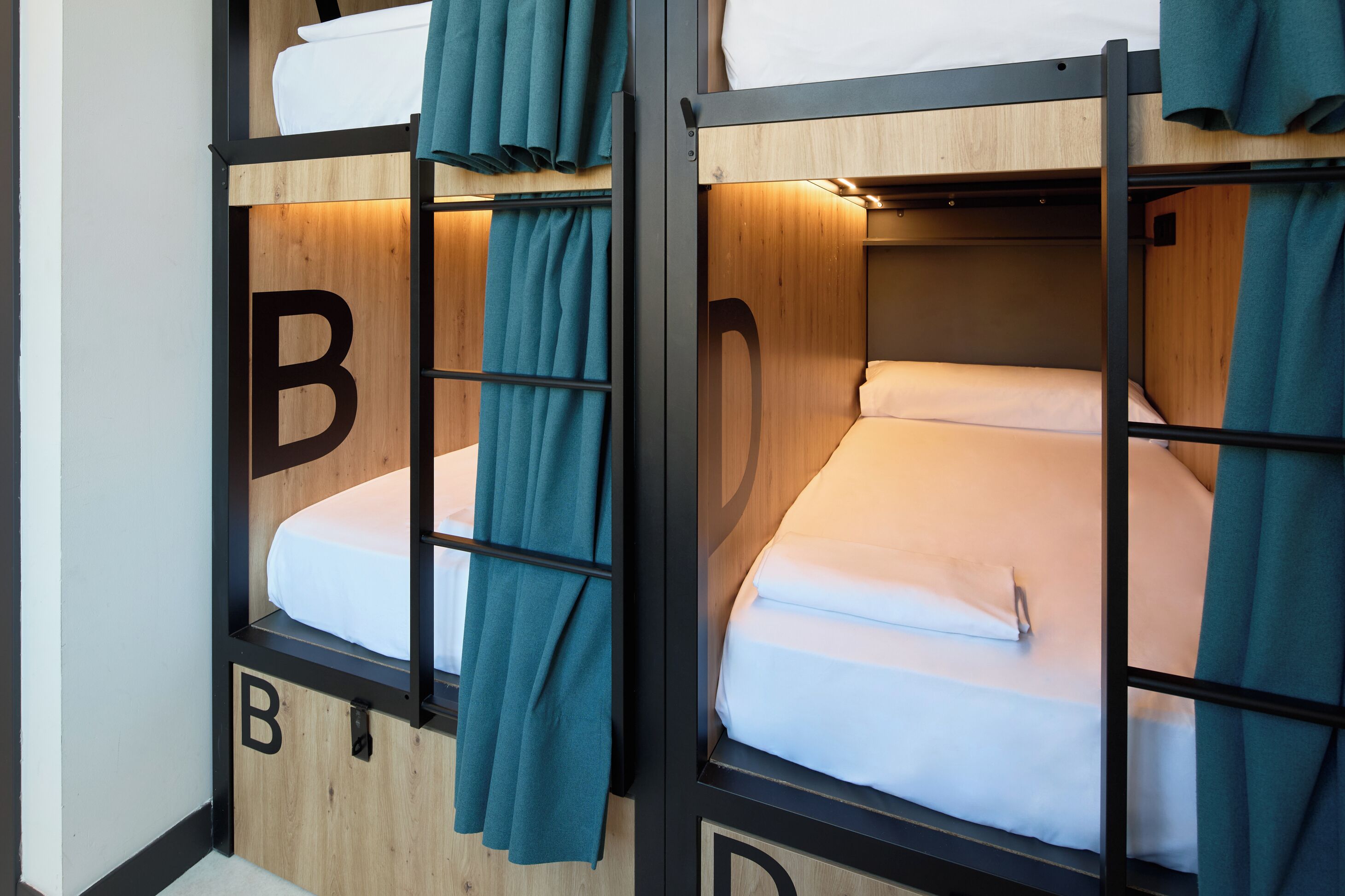 A bunk bed with a wooden frame and teal curtains, labeled with the letter 'B'.