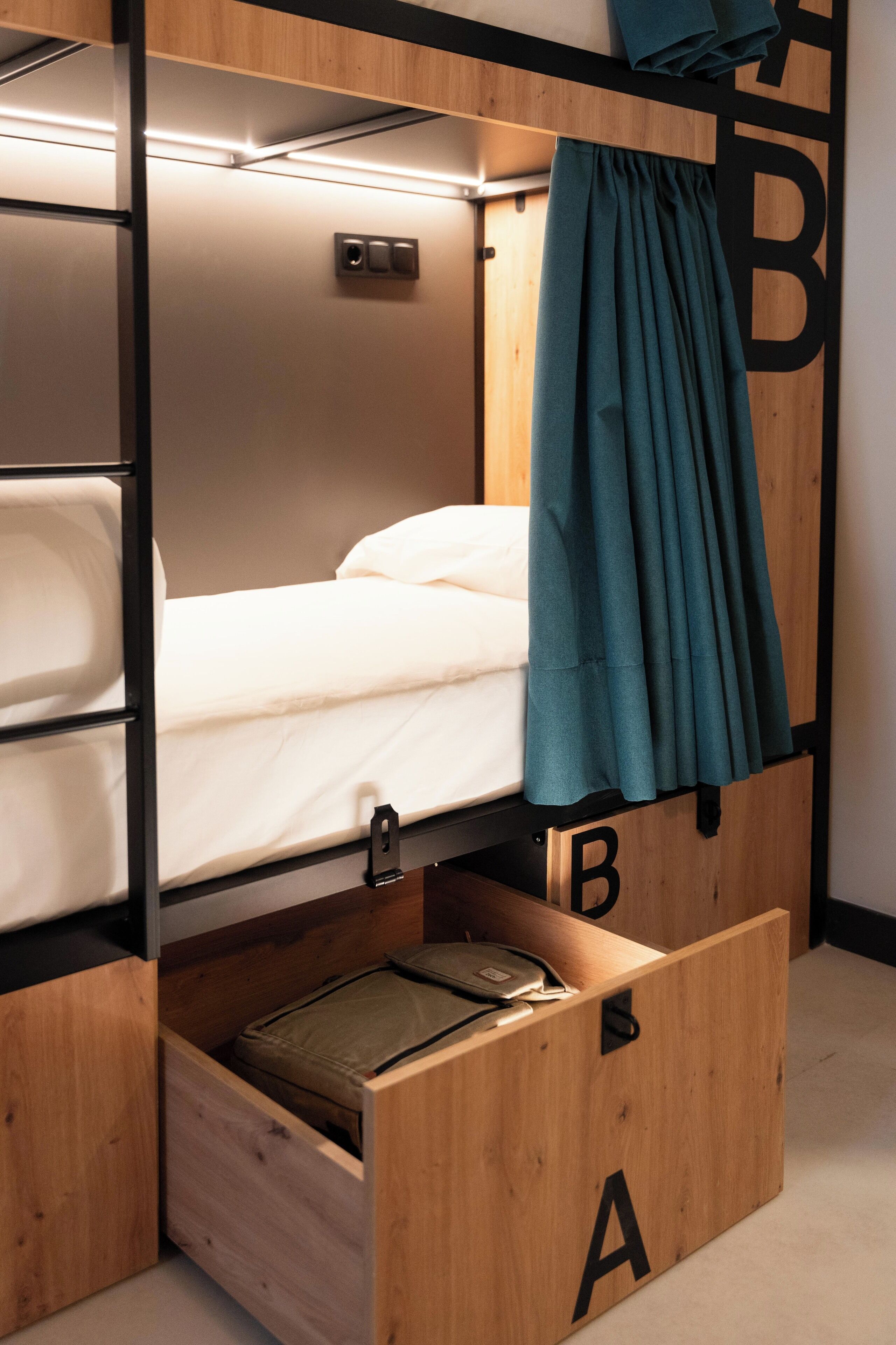 Habitación compacta y moderna con literas, un armario de madera con compartimentos etiquetados A, B y C, y una pequeña zona de escritorio.