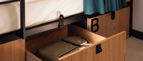 Habitación compacta y moderna con literas, un armario de madera con compartimentos etiquetados A, B y C, y una pequeña zona de escritorio.