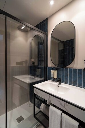 Een moderne badkamer met een douchecabine van glas, een witte wastafel met een zwarte kraan, en een grote spiegel.