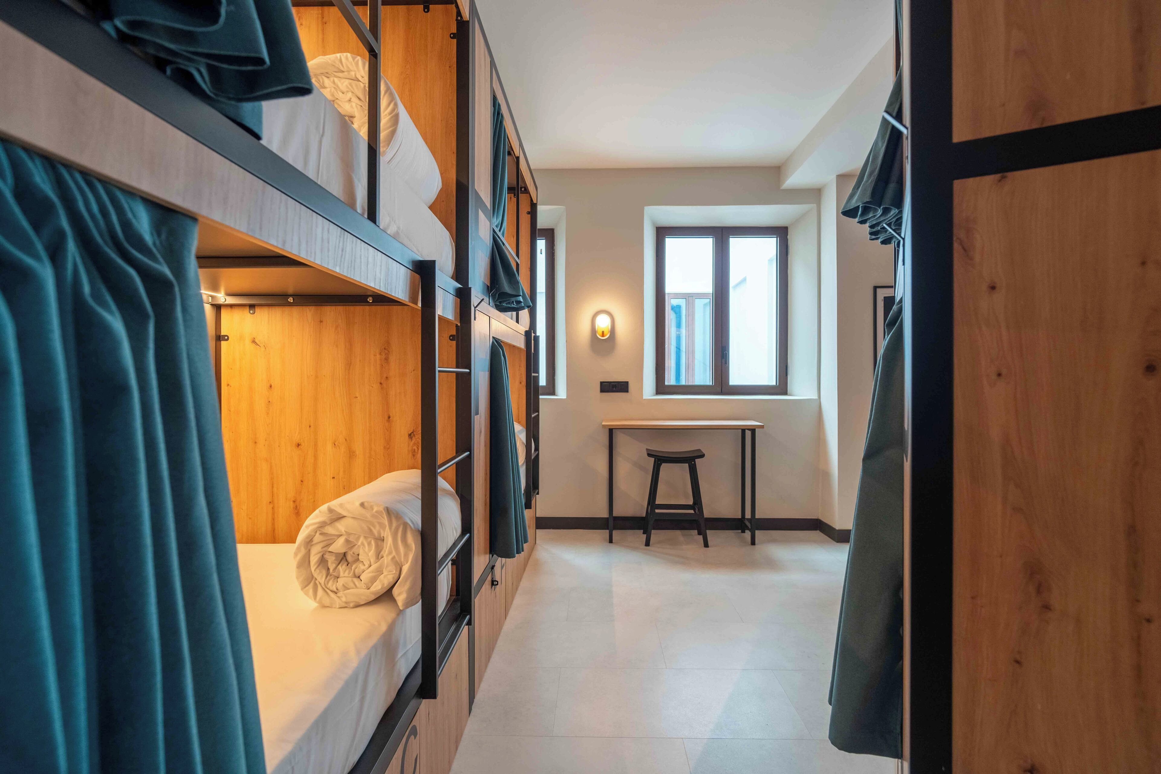 A dormitory room with bunk beds, a desk, and a window.