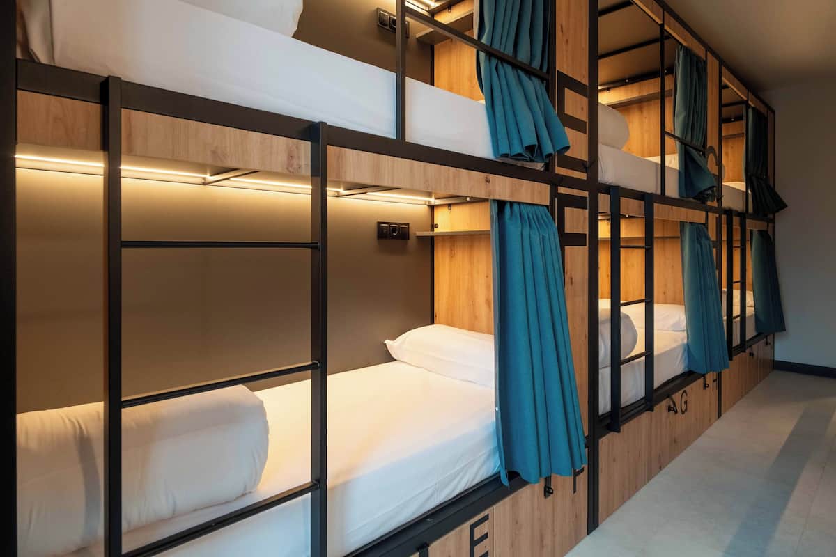 Une chambre avec un lit superposé, des murs en bois, des barreaux en métal et du linge de lit blanc.