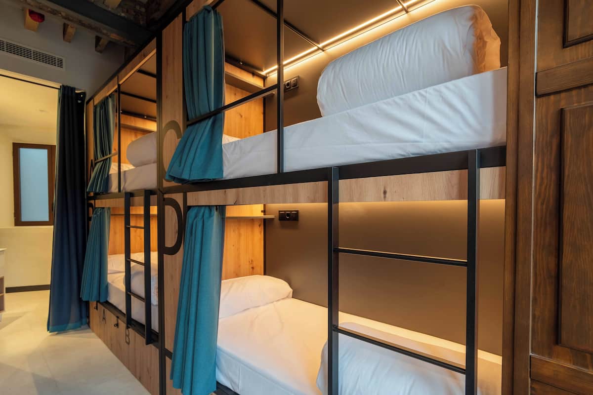 Une chambre avec un lit superposé, une tête de lit en bois, une petite étagère et un rideau.