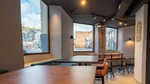 A modern interior with large windows, tables, and benches. - The Central House Granada Elvira Hostel (Granada)