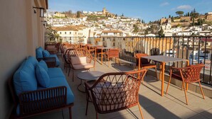 A balcony with wicker furniture, a sofa, and a view of a town with buildings and a tower. - The Central House Granada Elvira Hostel (Granada)