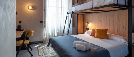 A bunk bed room with a desk, chairs, and a patterned rug.