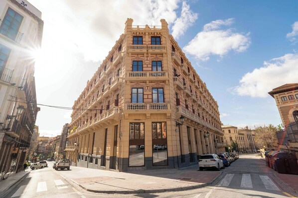 A multi-story building with a central entrance, balconies, and a street view.
