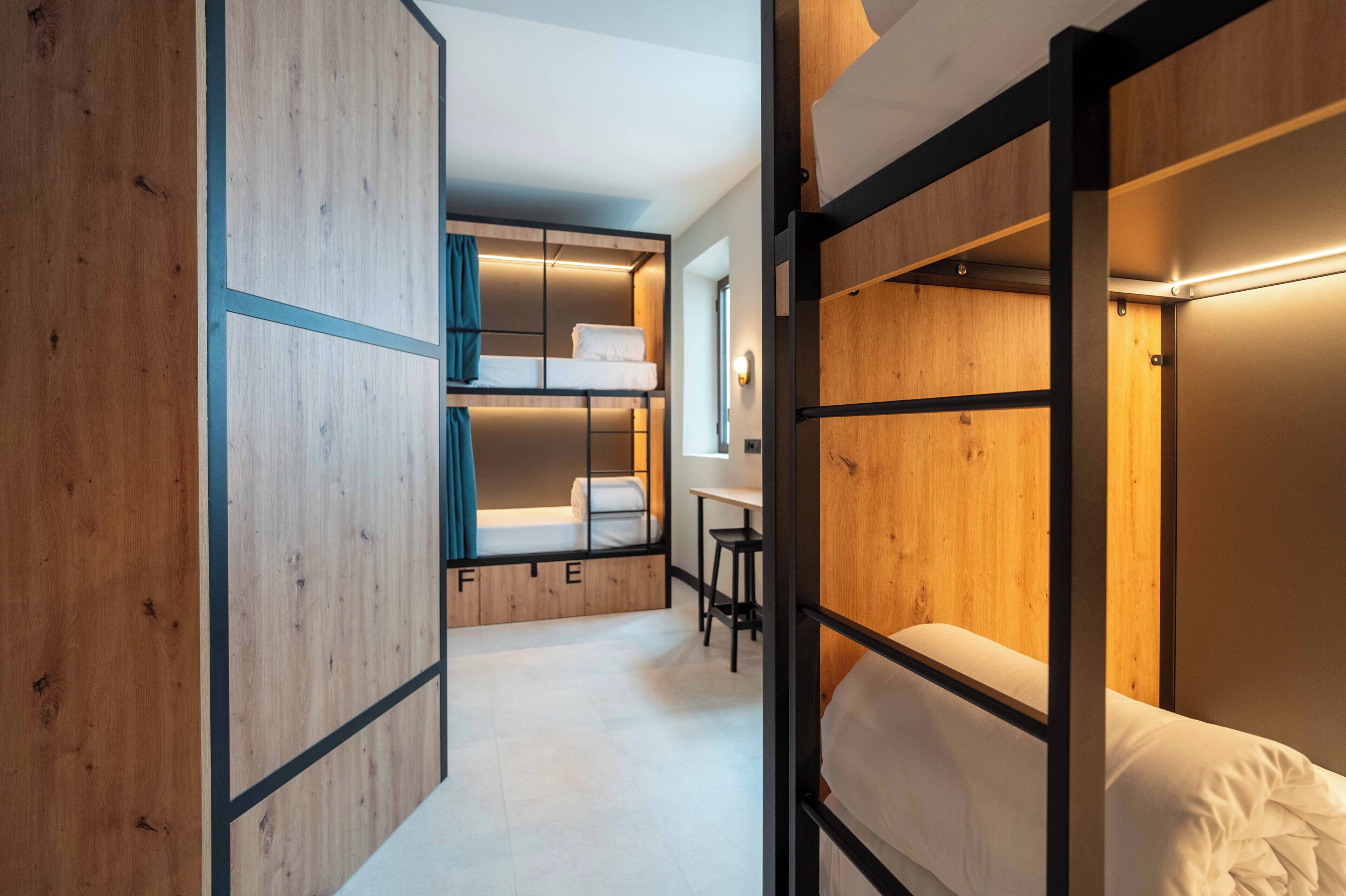 A compact hotel room with bunk beds, a small desk, and a window.