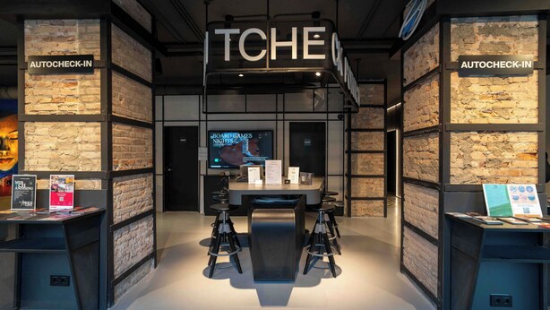 A modern interior with a central table, bar stools, and signs indicating 'AUTOCHECK-IN' on both sides. - The Central House Granada Elvira Hostel (Granada)